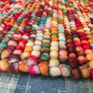 Puede incluir: Una colorida alfombra con superficie texturizada. La alfombra está hecha de fibras redondeadas y densamente empaquetadas en una variedad de colores, incluyendo rojo, naranja, amarillo, verde, azul y morado. Las fibras están dispuestas en filas verticales.