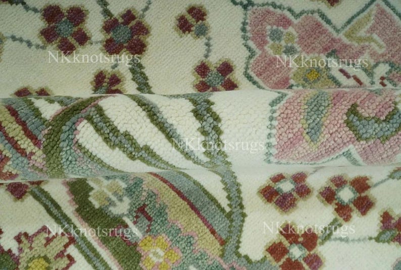 May include: Close-up of a rolled rug with a floral design. The rug has a cream background with repeating floral patterns in pink, burgundy, green, and yellow. The text "NKknotsrugs" is visible.
