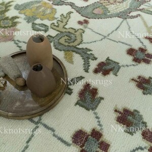 May include: A close-up of a decorative rug with a floral pattern in shades of cream, green, and burgundy. A wooden tray holds three brown vases and decorative items. The rug has a detailed design.