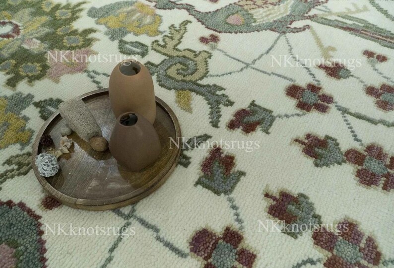 May include: A close-up of a decorative rug with a floral pattern in shades of cream, green, and burgundy. A wooden tray holds three brown vases and decorative items. The rug has a detailed design.