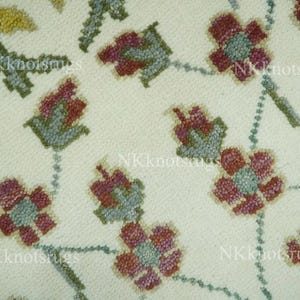 May include: Close-up of a cream-coloured rug with a floral pattern. The design features stylised flowers in shades of burgundy and teal, connected by a dotted vine pattern. The rug's texture is visible, suggesting a woven or embroidered construction.
