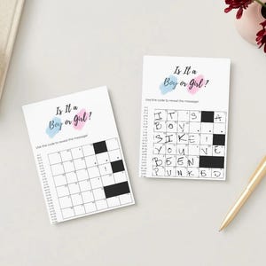 May include: Two gender reveal crossword puzzles on a white surface. The top of each card reads "Is It a Boy or Girl?" with blue and pink watercolor accents. One puzzle is solved, revealing "SIKE! You've Been Punked."