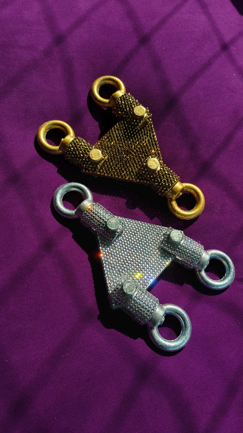 May include: Two triangular metal hardware connectors, one in gold tone and one in silver tone, both fully encrusted with small sparkling rhinestones. Each piece features three circular loops at the corners and three small metal bolts on the surface.