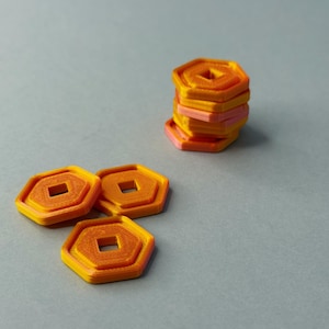 Può includere: Una collezione di oggetti esagonali arancioni e rosa con un foro quadrato al centro. Alcuni sono impilati, altri sparsi su una superficie grigia. Gli oggetti hanno un design a strati, creando un effetto tridimensionale. La sfumatura di colore aggiunge interesse visivo.