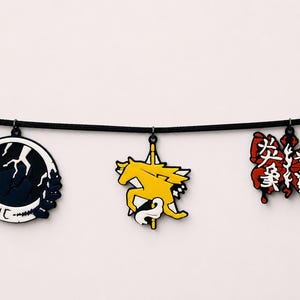 Puede incluir: Tres dijes decorativos colgando de un cordón negro. El dije de la izquierda es un emblema circular en blanco y negro con un rayo. El dije central es un caballo amarillo sobre una estrella. El dije de la derecha es una mariposa roja con texto japonés blanco.