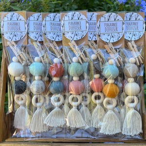 May include: A display of colorful fragrance diffusers. Each diffuser features a felt ball, wooden beads, a wooden ring, and a tassel. The diffusers are packaged in clear plastic with a tag that reads "FRAGRANCE DIFFUSER".
