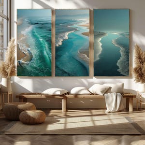 May include: Three framed prints depicting a coastal scene with turquoise and blue ocean waves. The artwork shows the waves breaking on the sandy shore. The frames are a natural wood colour, enhancing the coastal theme and adding warmth to the room.