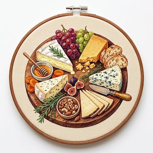 Puede incluir: Un bastidor de bordado circular con un diseño detallado en punto de cruz de una tabla de quesos. La tabla muestra trozos de varios quesos, uvas rojas y verdes, higos, un cuenco de miel con un cucharón, nueces y rebanadas de pan.