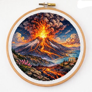 May include: A circular wooden embroidery hoop containing a cross-stitch piece depicting a volcanic eruption. The scene features a mountain with flowing lava, a plume of dark smoke, a coastal landscape with buildings, and pink flowers in the foreground.