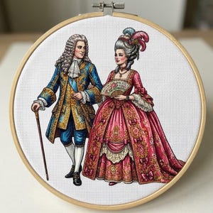 May include: A circular wooden embroidery hoop containing a cross-stitch design of a couple in 18th-century attire. The figure on the left wears a blue and gold coat with a wig and cane. The figure on the right wears a pink gown and holds a fan.