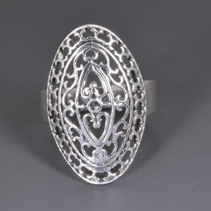 Puede incluir: Un anillo plateado con un diseño de filigrana ovalado. El anillo presenta un patrón calado con intrincados remolinos y motivos florales. La banda es de plata maciza. Es una pieza de joyería.
