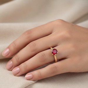 Peut inclure: Une bague en or ornée d'une grosse pierre précieuse rouge vif et ronde. La bague est sertie sur un fin anneau en or, mettant en valeur la couleur et l'éclat de la pierre. Un design classique, adapté à diverses occasions.