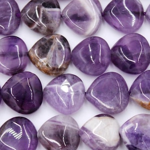 May include: Close-up of a strand of polished amethyst beads. The beads are a deep purple color with white and brown inclusions. Each bead is smooth and rounded, with a heart-like shape. The beads are strung together on a purple cord.