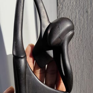 Peut inclure: Une sculpture en bois brun foncé représentant une figure abstraite. La sculpture a une forme incurvée et allongée avec une finition lisse et polie. La figure semble être assise ou à genoux, avec une tête arrondie et un dos courbé.