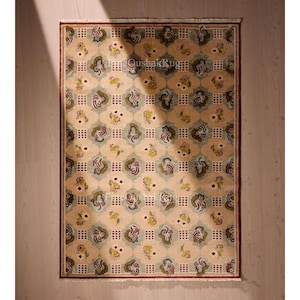 May include: Rectangular beige rug with a repeating pattern of floral and geometric shapes in shades of green, yellow, and red. The rug has a dark red border and a light beige background. The text "TheQushakRug" is visible.