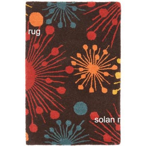 May include: A rectangular rug with a dark brown background and a repeating pattern of colorful starburst designs in orange, red, yellow, and teal. The word "rug" is visible in the image.