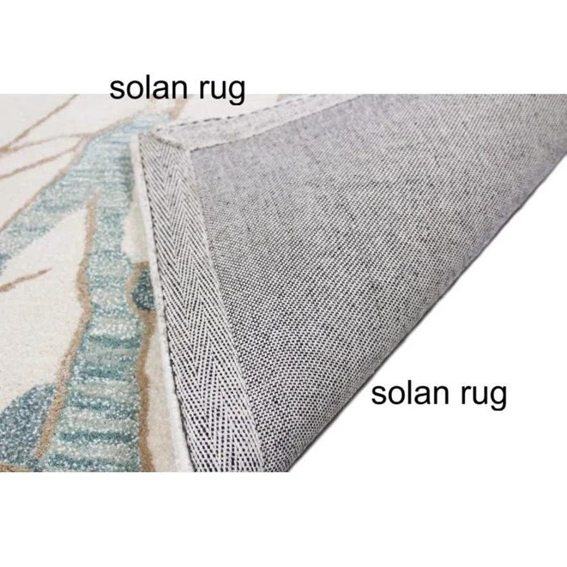 May include: A section of a rug with a floral design in shades of blue, beige, and white. The underside of the rug is gray, and the text "solan rug" is visible in two places.