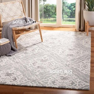 May include: A rectangular area rug with a gray and white pattern. The rug has a distressed, vintage look. The rug is in a room with a wooden chair and a window.