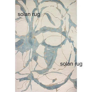 May include: Rectangular rug with a cream background and a blue and tan abstract design. The rug has the words "solan rug" printed on it.