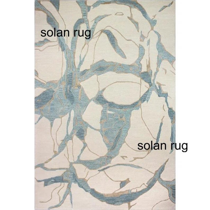 May include: Rectangular rug with a cream background and a blue and tan abstract design. The rug has the words "solan rug" printed on it.