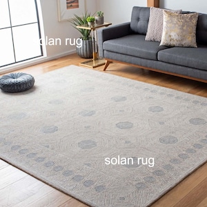 May include: A light grey area rug with a geometric pattern, featuring a repeating design of hexagons and circles. The rug has a border with a similar pattern. The text "solan rug" is visible on the rug.