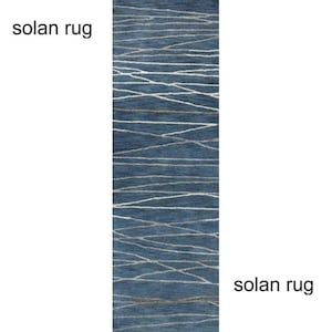 May include: A rectangular blue rug with a white and gold linear pattern. The rug has the text "solan rug" on the top and bottom. The rug is a home decor item.