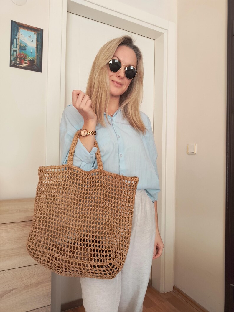 May include: A large, rectangular, tan-colored tote bag crafted from a coarse, open-weave natural fiber material. The bag features two sturdy, matching woven handles at the top and a spacious, unlined interior compartment with a visible grid pattern.