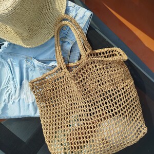 May include: A tan woven straw tote bag with an open mesh design and two top handles, accompanied by a matching tan woven straw hat and a pair of light blue distressed denim shorts with frayed edges and visible white pocket lining.