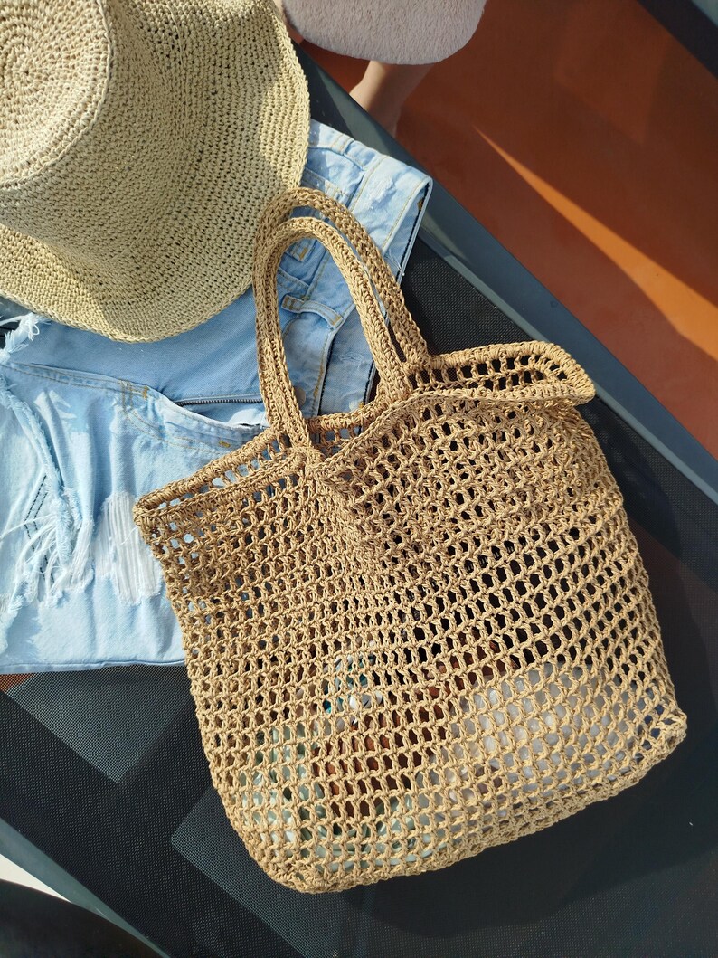 May include: A tan woven straw tote bag with an open mesh design and two top handles, accompanied by a matching tan woven straw hat and a pair of light blue distressed denim shorts with frayed edges and visible white pocket lining.