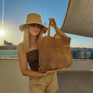 May include: A tan crochet bucket hat and a large, tan, open-weave crochet tote bag with two handles. The tote bag features a grid-like pattern and is constructed from a textured, fibrous material, showcasing a spacious, rectangular design.