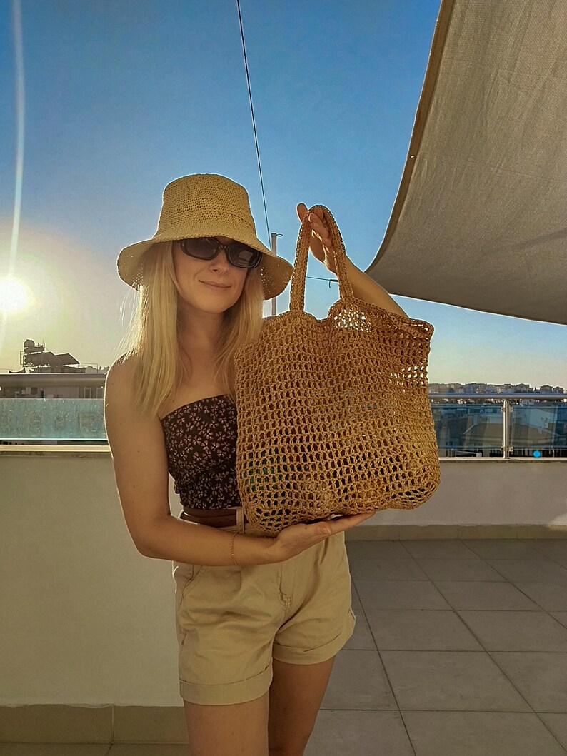 May include: A tan crochet bucket hat and a large, tan, open-weave crochet tote bag with two handles. The tote bag features a grid-like pattern and is constructed from a textured, fibrous material, showcasing a spacious, rectangular design.