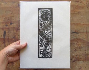 May include: Black and white linocut print of a snake with a patterned body, framed in a white mat and a clear plastic sleeve. The print is titled "Serpentine" and signed and dated.