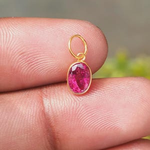 Op de afbeelding: Een kleine, gouden hanger met een levendige, ovaal geslepen, roze edelsteen. De hanger heeft een eenvoudig, elegant ontwerp met een lus aan de bovenkant voor een ketting. De edelsteen is gezet in een gouden bezel.