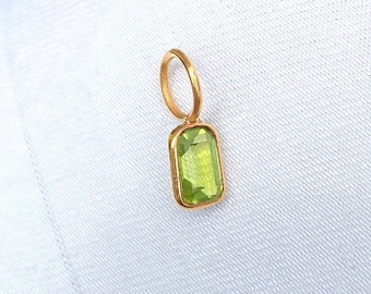 May include: A gold pendant featuring a rectangular, light green gemstone. The gemstone is set in a gold bezel and has a loop for a chain. The pendant is shown against a white backdrop.
