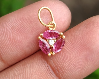 May include: A gold pendant featuring a cluster of three pink gemstones, each with a marquise cut, surrounding a central white gemstone. The pendant has a small loop for a chain.