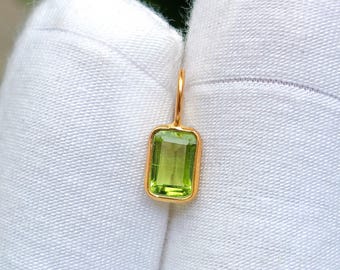 May include: A gold pendant with a rectangular, light green gemstone. The gemstone is set in a gold bezel, and the pendant has a small loop for a chain. The design is simple and elegant, suitable for everyday wear. The gemstone is approximately 1 cm in length.