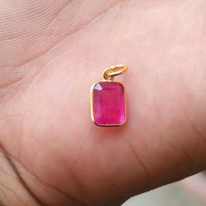 Peut inclure: Un pendentif rectangulaire avec une pierre précieuse rose vif sertie dans un cadre doré. Le pendentif a une boucle en haut pour une chaîne. La pierre précieuse est d'un rose profond et riche.