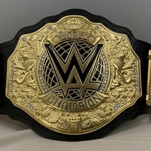 以下が含まれることがあります： 黒い革のストラップが付いた、金色のレスリングチャンピオンシップベルト。中央のプレートにはWWEのロゴと「WORLD CHAMPION」の文字が描かれています。ベルトは複雑なデザインで装飾され、小さな輝く石が埋め込まれています。