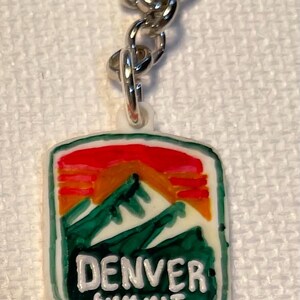 May include: A keychain with a rectangular pendant depicting a mountain scene in green, orange, and red. The text "DENVER SUMMIT FC" is in white. The keychain has a silver chain and ring.