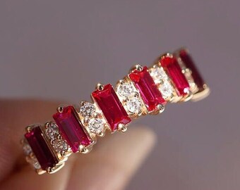 Könnte beinhalten: Ein goldener Ring mit abwechselnd rechteckigen roten und kleinen weißen Edelsteinen. Das Design des Rings wird vor einem verschwommenen Hintergrund hervorgehoben, wodurch die Edelsteine zur Geltung kommen.