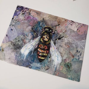 Puede incluir: Primer plano de una abeja pintada con rayas negras y amarillas, acentos rojos y alas blancas. La abeja est&aacute; sobre un fondo texturizado con tonos de morado, azul y marr&oacute;n.