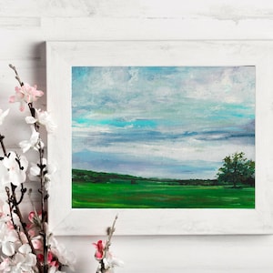 May include: A framed painting of a landscape with a green field, a single tree, and a cloudy sky. The sky is a mix of blue, white, and gray.