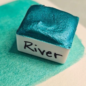 以下が含まれることがあります： ラベルに「River」と書かれたターコイズブルーのメタリック水彩絵の具パレット