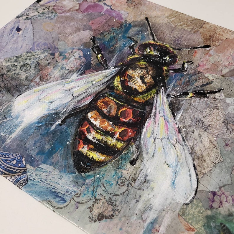 Puede incluir: Primer plano de una abeja pintada con rayas amarillas y negras, acentos rojos y alas blancas. La abeja est&aacute; sobre un fondo texturizado con tonos azules, grises y morados.