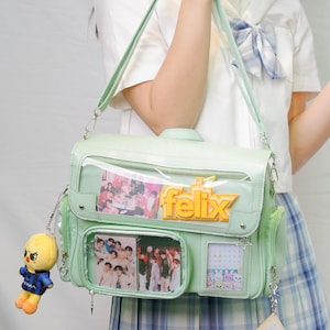 May include: A pale green satchel bag with a clear window showing a group photo and the name "felix" in yellow. The bag has a small yellow plushie attached to the side.
