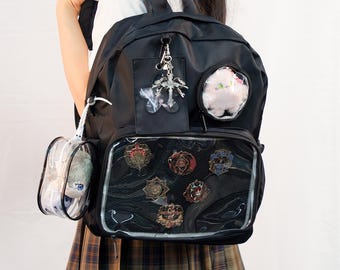 May include: Black backpack with clear pockets showcasing decorative pins and a plush toy. The bag features a silver charm and a small clear pouch. The backpack is worn by a person wearing a plaid skirt.