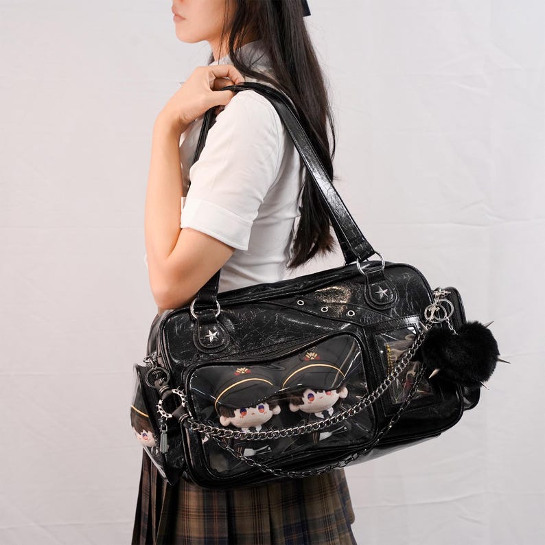 May include: Black patent leather shoulder bag with star accents and clear pockets displaying plush dolls. The bag features a chain and a black pom-pom charm. The bag has a top handle and a shoulder strap.