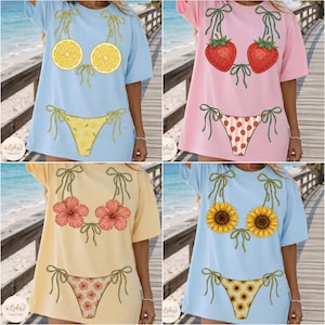 May include: Four t-shirts with bikini designs. The shirts are light blue, pink, yellow, and light blue. The bikini tops and bottoms feature lemon slices, strawberries, hibiscus flowers, and sunflowers. The bikini tops have green bow ties.