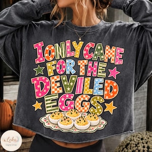 May include: A charcoal grey crewneck sweatshirt featuring the colourful text I ONLY CAME FOR THE DEVILED EGGS in various patterns like polka dots and checkers. Below the text is a graphic of a white platter holding five deviled eggs.