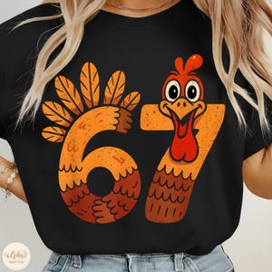 May include: Black t-shirt featuring a Thanksgiving-themed graphic. The design includes the numbers "67" stylized as a turkey, with orange and brown feathers and a red wattle. The shirt is a festive apparel item.
